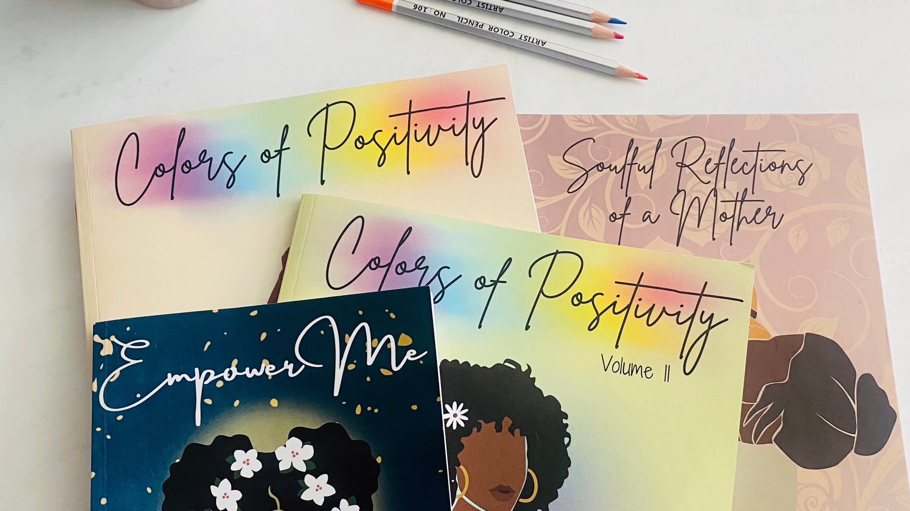 Journals titled 'Colors of Positivity' and 'Empower Me' with coloring pencils on a white surface.